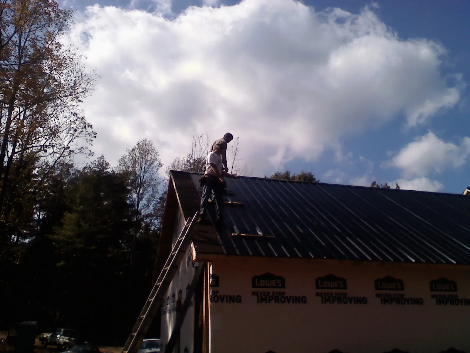 Roofer fastening dark metal panels high against a cloudy sky, from a Roof Inspection job in Waterbury